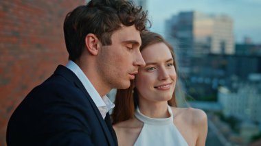 Akşam vakti çatıda dikilen çiftler yakın plan çekimde. Romantik ruh eşleri konuşarak gülerek alacakaranlıkta mutlu anların tadını çıkarıyorlar. Şık gülümseyen eşler restoran terasında şehrin alaca karanlığına bakıyor..