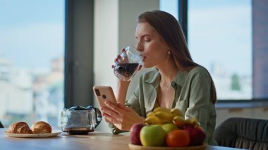 Kahvaltı masasında espresso içen sakin bir kadın akıllı telefonu yakından izliyor. Rahat kız sabah ışığında online iletişimden keyif alıyor. Gülümseyen esmer, cep telefonlu, dairede kahve yudumlayan.