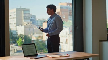 Başarılı CEO, ofis panoramik penceresini kapatıyor. Ciddi bir iş adamı cep telefonuyla iş konuşmasından sonra şehir manzarası izliyor. Modern şirket odasında kariyer üzerine zengin bir yönetici düşüncesi.