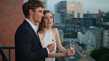 Şampanya eşliğinde flört eden güzel bir çift. Lüks kıyafetler içinde gülümseyen eşler restoran terasında romantik bir akşamın tadını çıkarıyorlar. Mutlu çift şarap kadehleriyle şehir manzarasını seyrediyor..
