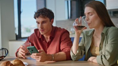 Heyecanlı eşler akıllı telefondan mesaj okuyor ve yakın planda birlikte kahvaltı ediyorlar. Duygusal çift mutfakta kahve içerken cep telefonundan harika haberler alıyor. Neşeli aile mutlu hissediyor..