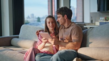 Romantik çift, rahat kanepe dairesine yakın çekim tableti. Gülümseyen evli çift evde bilgisayarla tatil yapmayı planlıyor. Mutlu ruh eşleri birlikte sosyal medyayı izliyorlar..