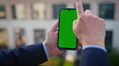 Ofis binasının arka planında yeşil ekran akıllı telefon var. Modern mahallede insan kullanıcısı cep telefonuna dokunuyor. Kromakey cep telefonu kullanan tanınmayan patron yöneticisi