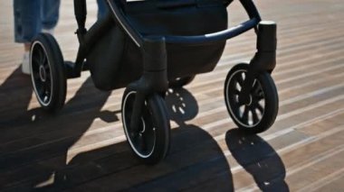 Ebeveynlerin bacakları, yeni doğmuş bir bebekle sokak güneşinde bebek arabasında yürüyor. Karı koca yürürken gülümserken mutlu hisseder. Rahat, neşeli bir çift sabah çocuk arabası sürüyor. Ebeveynlik kavramı