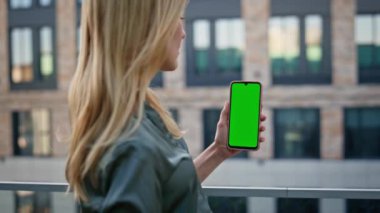 İş kadını yeşil ekran akıllı telefonuyla sokak kapanışında video görüşmesi yapıyor. Sarışın yönetici cep telefonundan iş mesajı okuyor. Göz kamaştırıcı bayan web sitesi açık havada kroma tuşlu telefonda