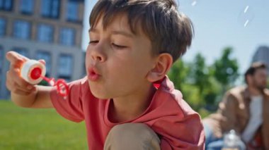 Küçük çocuk dışarıdaki sabun köpüklerini yakından çekmeyi seviyor. Gülümseyen küçük çocuk yaz tatilini yeşil bölgede geçiriyor. Yeşil çayırda oynayan kaygısız neşeli çocuk. Mutlu çocukluk kavramı
