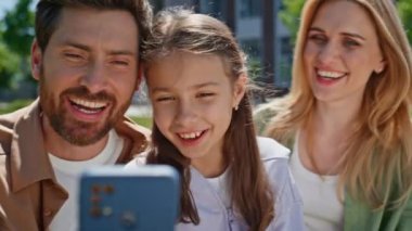 Gülümseyen ebeveyn kızı yazın internette akıllı telefon sallıyor. Mutlu kadın ve kız gün ışığı bahçesinde cep telefonu ekranına bakıyorlar. Ailenin temiz havada görüntülü görüşmesi var. 