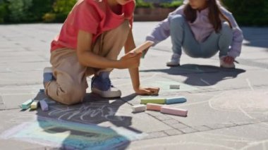 Güneşli oyun parkında tebeşir çizen küçük çocuklar. Küçük kardeş birlikte oynuyor yaz tatillerinde renkli pastel boyalarla resimler yapıyor. İki arkadaş rahat bir mahallede vakit geçiriyorlar.