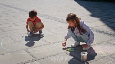 Güneşli sokakta boya kalemleri çizen iki çocuk. Yerde oturup çizim yapan sevimli çocuklar. Küçük erkek ve kız kardeş yaz mahallesinde birlikte vakit geçiriyorlar. Mutlu çocukluk kavramı