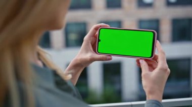 Eller şehirde yatay kromakey cep telefonunu tutuyordu. Yeşil ekranda haber okuyan kimliği belirsiz bir kadın. Şehir merkezinde isimsiz bir yönetici dinleniyor. Sarışın patron görünümlü