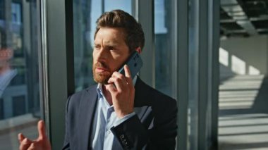 Sakallı CEO cep telefonu konuşan modern mimari bina. Esmer iş adamı iş portresi için ortaklarını arıyor. Panoramik Pencere Ofisi 'nde akıllı telefondan konuşan zarif patron.