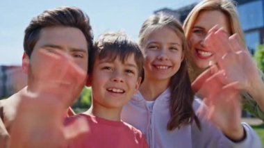 Yeşillik mahallesine el sallayan güzel bir aile. Web kamerasına gülümseyen mutlu ebeveynlerin ve çocukların portresi. Çevrimiçi yakınlarından bahseden neşeli insanlar 