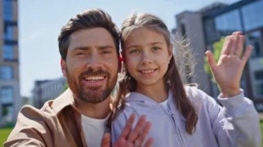 Baba kız el sallayarak yeşillik mahallesine bakıyor. Web kamerasına gülümseyen mutlu ebeveyn ve çocuk portresi. Yakın plan neşeli baba ve kız internette akrabalarıyla konuşuyor. 