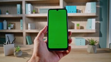 Freelancer görünümlü yeşil ekran akıllı telefon. Uzak iş yerinde çalışıyor. Yakınlaştır. Bilinmeyen işadamı Chroma Key cep telefonundaki çevrimiçi içeriğe göz atıyor. Modelleme telefonunda video izleyen adam yöneticisi.