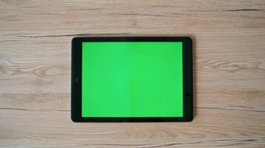 Üst görüntü yeşil ekran tableti, uzak iş yerinde yakın plan. Ahşap masanın üzerinde krom anahtar bilgisayarı olan boş bir şirket çalışma alanı. Daire masasına modern yatay dijital aygıt yerleştirildi.