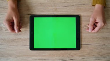 Evdeki masadaki Chromakey Tablet 'te video izleyen bir bayan. Bilinmeyen iş kadını ofisteki yeşil ekranlı bilgisayara göz atıyor. Şablon cihazının yanındaki tahta masada yatan kadın elleri.