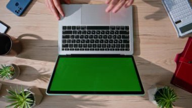 Ev ofisinin üst görüntüsünde krom anahtar dizüstü bilgisayarda çalışan uzak bir yönetici. İşadamı masadaki yeşil ekran bilgisayarda e-postaları karıştırıyor. Bilinmeyen bağımsız modelleme aygıtında online araştırma yapıyor
