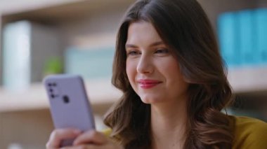 Şirketimizin iş yerinde cep telefonu okuyan neşeli bir kız. İş yerinde gülümseyen akıllı telefon ekranlı çekici bir kadın. Pozitif iş kadını cep telefonu çevrimiçi iletişimini seviyor.