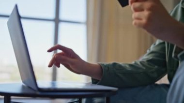 Büyük pencerelerden laptop alan bir adam var. Geniş apartmandaki uzaktan satın alma düğmesine basmak için kart tutan mutlu serbest yazar. Başarılı internet ödeme kavramı