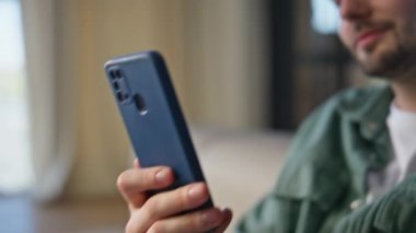 Kullanıcı evde akıllı telefonu yakın çekimde tutuyor. Evde rahatlarken cep telefonu videosu izleyen mutlu ve rahat bir adam. Esmer adam cep telefonu ekranında sadece sosyal ağlar uygulamasını kullanarak e-kitap okuyor.