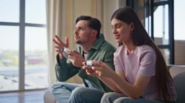 Apartman dairesinde oyun oynayan arkadaşlar online yarışmanın keyfini çıkarıyorlar. Kablosuz konsollar tutan duygusal erkek kız sevinçle kazanıyor. Mutlu sevgili kanepeye zıplayarak başarıyı kutluyor.