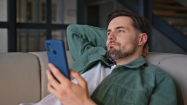 Rahat adam, rahat bir kanepede uzanmış akıllı telefonu izliyor. Gülümseyen yakışıklı adam cep telefonu ekranında sinemadan zevk alıyor. Neşeli serbest yazar rahat bir kanepede tek başına dinleniyor. 