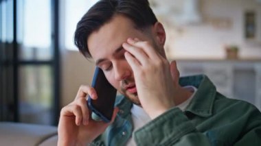 Modern apartman dairesinde akıllı telefondan konuşan yorgun bir adam. Portre yorgun, çekici bir adam ciddi bir telefon konuşması yapıyor. Tıraşsız erkek akıllı telefon görüşmesinde sorun yaşıyor. 