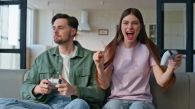 Apartman kapanışında video oyunu oynayan gençler. Online yarışmayı kazanan kadın. Kablosuz konsolu tutan duygusal kız kendini mutlu hissediyor. Üzgün erkek arkadaş oturma odasında hayal kırıklığına uğramış surat yapıyor.