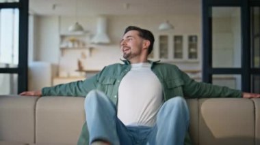 Kanepeye düşen sıradan bir adam. Yakın çekimde rahatlamış hissediyor. Keyfi yerinde gülümseyen kaygısız bir adam. Oturma odasında eğleniyor. Rahat bir dairede tek başına istirahat eden serbest çalışan mutlu bir kanepe.