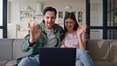 Aşırı mutlu çiftin laptopla duygusal bir video konferansı yapması. Rahat çift hafta sonları koltukta oturup eğleniyor. Neşeli gülen eşler video konferansında vakit geçiren arkadaşlarına hikayeler anlatıyor.