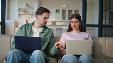 Oturma odasındaki iç mekanda çalışan iki bağımsız bilgisayar. Ciddi bir eş dizüstü bilgisayarları birlikte yazıyor. Uzak işyerindeki internet işinden keyif alan odaklanmış aile siteleri