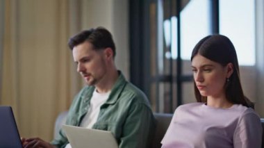 Oturma odasındaki kanepede dizüstü bilgisayarlara göz atan insanlarla ilgili. Bilgisayarda klavye yazan ciddi bir kadın. Koltuktaki görevlere odaklanmış. Genç çift rahat bir apartman dairesinde birlikte çalışıyor. 