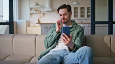 Neşeli hipster evde kameralı akıllı telefonlara bakarak sanal sohbetten bahsediyor. Gülümseyen yakışıklı adam hafta sonu cep telefonuyla konuşuyor, dinleniyor. Mutlu dost canlısı adam online webcam toplantısını seviyor