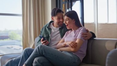 Akıllı telefonlu bir kadın ev koltuğunda çok başarılı görünüyor. Duygusal erkek arkadaş, esmer kız arkadaşına cep telefonunu gösteriyor ve duygularını paylaşıyor. Neşeli çift kazanan piyango evde dinleniyor.
