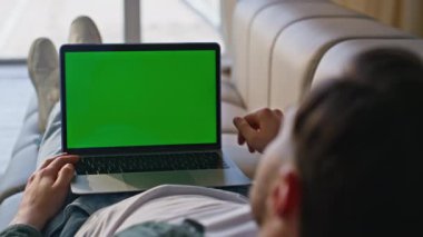 Freelancer ev kanepede yatarken dizüstü bilgisayar kullanıyor. Dairedeki kanepede duran yeşil ekran bilgisayardaki bilinmeyen adam tıkırdıyor. Uzaktan kumanda yöneticisi kapalı alanda krom anahtar dijital aygıt üzerinde çalışıyor 