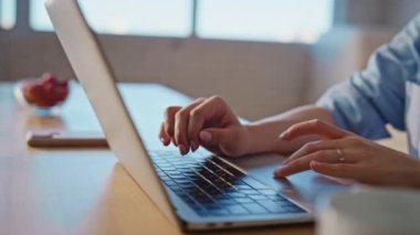 Eller sabah yakın planda ev masasında dizüstü bilgisayara basıyor. Modern mutfak işyerinde bilgisayar kullanan odaklı bir kadın. Rahat çalışma alanında internet araştırması yapan serbest çalışan bir kadın.