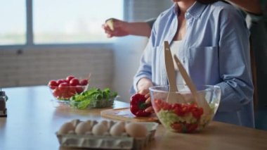 Ev hanımı elleri yakın çekimde tahta tahtada kırmızı dolma biber doğruyor. Genç adam karısının gözlerini kapayıp mutfakta sürpriz yapıyor. Sevgi dolu bir çift daire mutfağında şefkatle yemek pişiriyor.