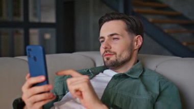 Akıllı telefondan kanepe yazıp ev ortamını yakından izleyen yalancı bir adam. Rahat iç mekanda cep telefonuyla dinlenen pozitif ssm çalışanı. Evcil erkek model, gün ışığında yalnız başına dinleniyor. 