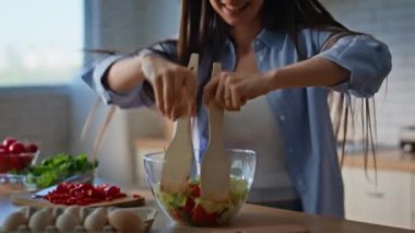 Ev hanımı elleri mutfakta salata karıştırıyor. Kulaklıkla dans eden neşeli kız organik öğle yemeği için taze malzemeler hazırlıyor. Mutlu kadın kablosuz kulaklıkla müzik dinlemekten hoşlanır. 