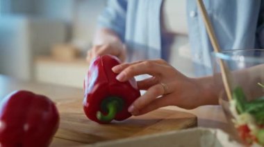 Ev mutfağında biber dilimleyen kadın elleri. Yakın plan. Gülümseyen kadın, apartman mutfağında bıçakla taze vitamin malzemeleri hazırlıyor. Aşçı öğle yemeği için sağlıklı sebze yemeği kesiyor. 