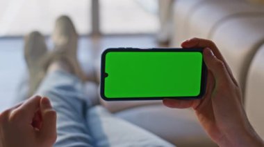 Evdeki krom anahtarlı akıllı telefonu yakından dinliyoruz. Kimliği belirsiz adam yeşil ekranlı cep telefonu kullanıyor. Oturma odasında dinleniyor. Apartman kanepesinde cep telefonu uygulamasını tarayan tanınmayan bir adam.