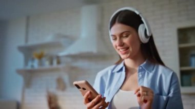 Mutfakta akıllı telefon kullanan bir kadın yemek pişirirken mesaj okuyor. Kulaklıklı neşeli bir kadın müzik açıyor. Kulaklıklı gülümseyen kız cep telefonuyla aşçılığın tadını çıkarıyor.