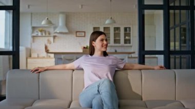 Neşeli model kanepede oturup gülümsüyor. Tasasız mutlu kadın hafta sonunun keyfini çıkarıyor. Rahatlamış hissediyor. Tembel kadının apartman dairesinde boş vakit geçirmesi. Yurt içi yaşam tarzı 
