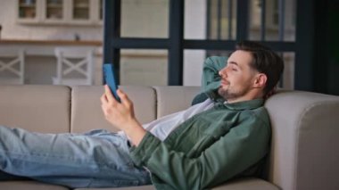 Rahat bir adam, evde rahat bir şekilde uzanan yeşil ekran akıllı telefonu izliyor. Mutlu adam serbest çalışıyor. Hücre molasında eğleniyor. Sakin iş adamı bej oturma odasında kromakey e-posta okuyor