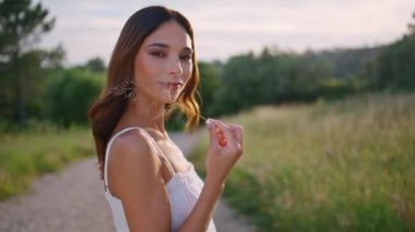 Kırsal kesimde kadın portresi. Kırsal kesimde çivi taşıyor. Yakın plan gülümseyen kadın yüzü ve akşam gökyüzü arka planında taze bahar bitkisi. Romantik model yola nazik bir dokunuşla bakıyor.