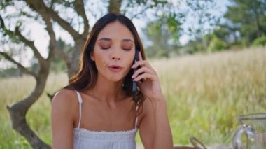 Kırsal model cep telefonu araması. Oturan ağaççı dükkanına yakın çekim. Ciddi bir kadın temiz hava doğasında akıllı telefondan bahsediyor. Rahat kız bahçede modern aletlerle yaz tatilinin tadını çıkarıyor. Teknoloji konsepti 