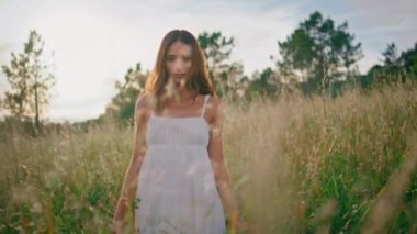 Tasasız kadın güzel bir yaz günü portresinde çayıra poz veriyor. Romantik, çekici bir kız. Ortalıkta dikilip sakin bir hafta sonunun tadını çıkarıyor. Beyaz elbiseli gülümseyen bayan sabah tarlasında dinleniyor. 