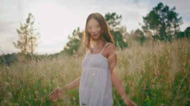 Tebessüm eden kadın, güneş ışığı portresi çiziyor. Kaygısız kadın altın kırsal alanda saçlarına dokunuyor. Beyaz elbiseli mutlu kız tek başına kameraya bakarak çekici hareketler yapıyor. 