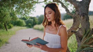 Doğada ağaçların altında dinlenen nazik bir kadın defter yazıyor. Esmer, rahat kadın, kitabı kapatıyordu. Kırsal kesimdeki portreye bakıyordu. Şehvetli model kız köyde poz veriyor. Halk konsepti 