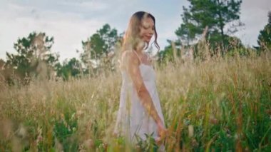 Rahatlamış bir kadın, yakın çiftlikteki dikenli çayırlarda geziniyor. Gülümseyen bayan sabah çayırında doğa yürüyüşünün tadını çıkarıyor. Tarım hasadında buğday saplarına dokunan dingin, güzel model el.